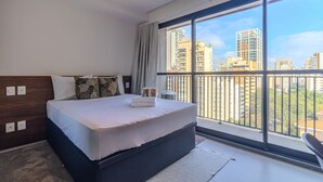 A modern bedroom with a large bed, a view of the city through a balcony, and a cityscape visible through the window. - Urbic Sabiá (São Paulo)