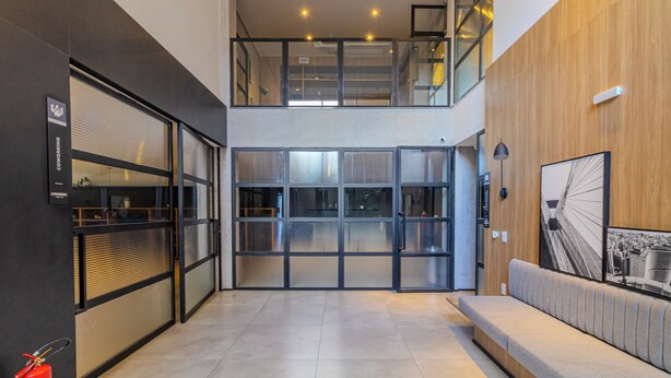 A modern interior with a glass door entrance, a fire extinguisher, a bench, and a framed picture on the wall. - Urbic Sabiá (São Paulo)
