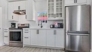A modern kitchen with white cabinets, stainless steel appliances, and a window with a red roof view.