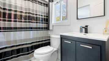 A bathroom with a striped shower curtain, a white toilet, a dark cabinet, a white countertop, a mirror, and a window with a view of trees.