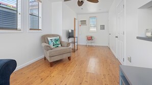 Une pièce dotée d’un ventilateur de plafond, d’un plancher en bois, d’un canapé avec un coussin, d’une petite table et d’une chaise.