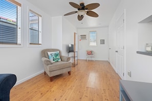 A room with a ceiling fan, wooden flooring, a sofa with a cushion, a small table, and a chair.