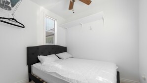 Une chambre à coucher comprenant un lit, un ventilateur de plafond, une fenêtre avec des stores et un climatiseur fixé au mur.