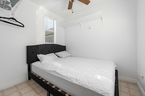 Une chambre à coucher comprenant un lit, un ventilateur de plafond, une fenêtre avec des stores et un climatiseur fixé au mur.