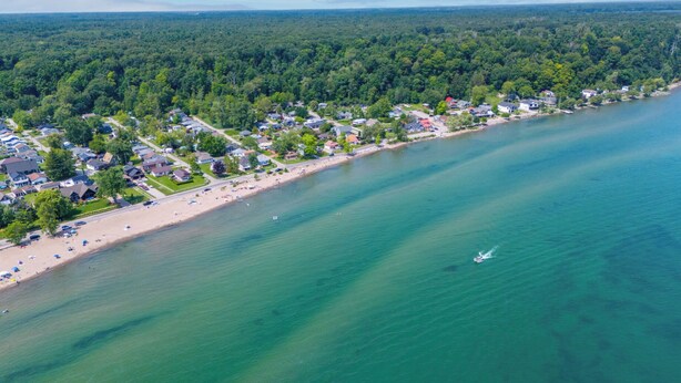 Vue aérienne d’une ville côtière avec une plage, des maisons et une zone boisée.