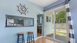 Une pièce comprenant un coin cuisine, deux tabourets, une porte-fenêtre coulissante donnant sur une terrasse et une pancarte indiquant « BIENVENUE À BORD ».