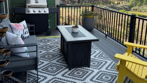 A deck with a grill, outdoor seating, and a view of a residential area.