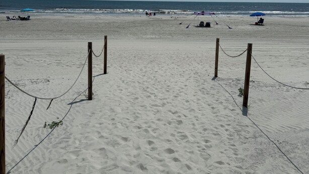 A sandy beach with a clear sky, wooden posts, and a rope barrier.