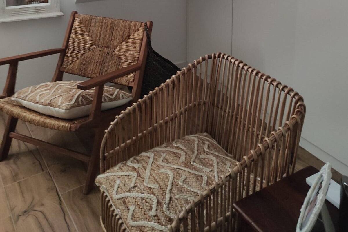 A room with a sloped ceiling, a wicker chair with a patterned cushion, and a wicker footrest.