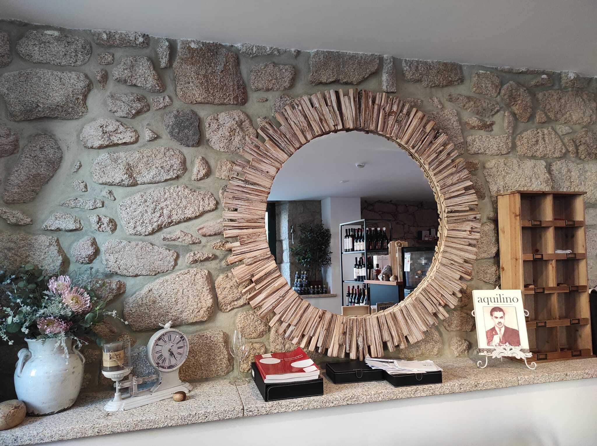 A stone wall with a circular mirror, a clock, a vase with flowers, and a sign with a name.