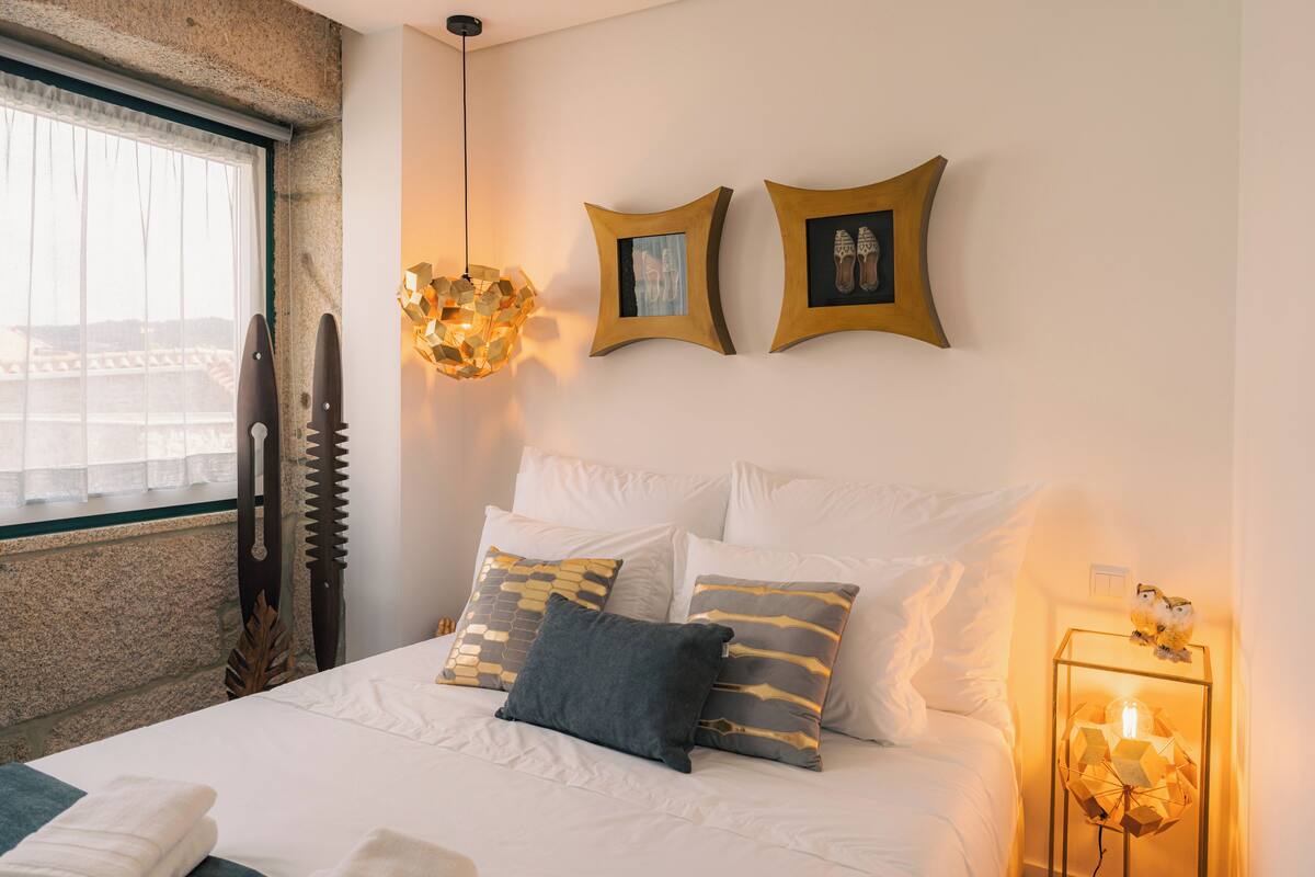 A neatly made bed with white and gold pillows, a wooden headboard, and a wall-mounted picture frame.