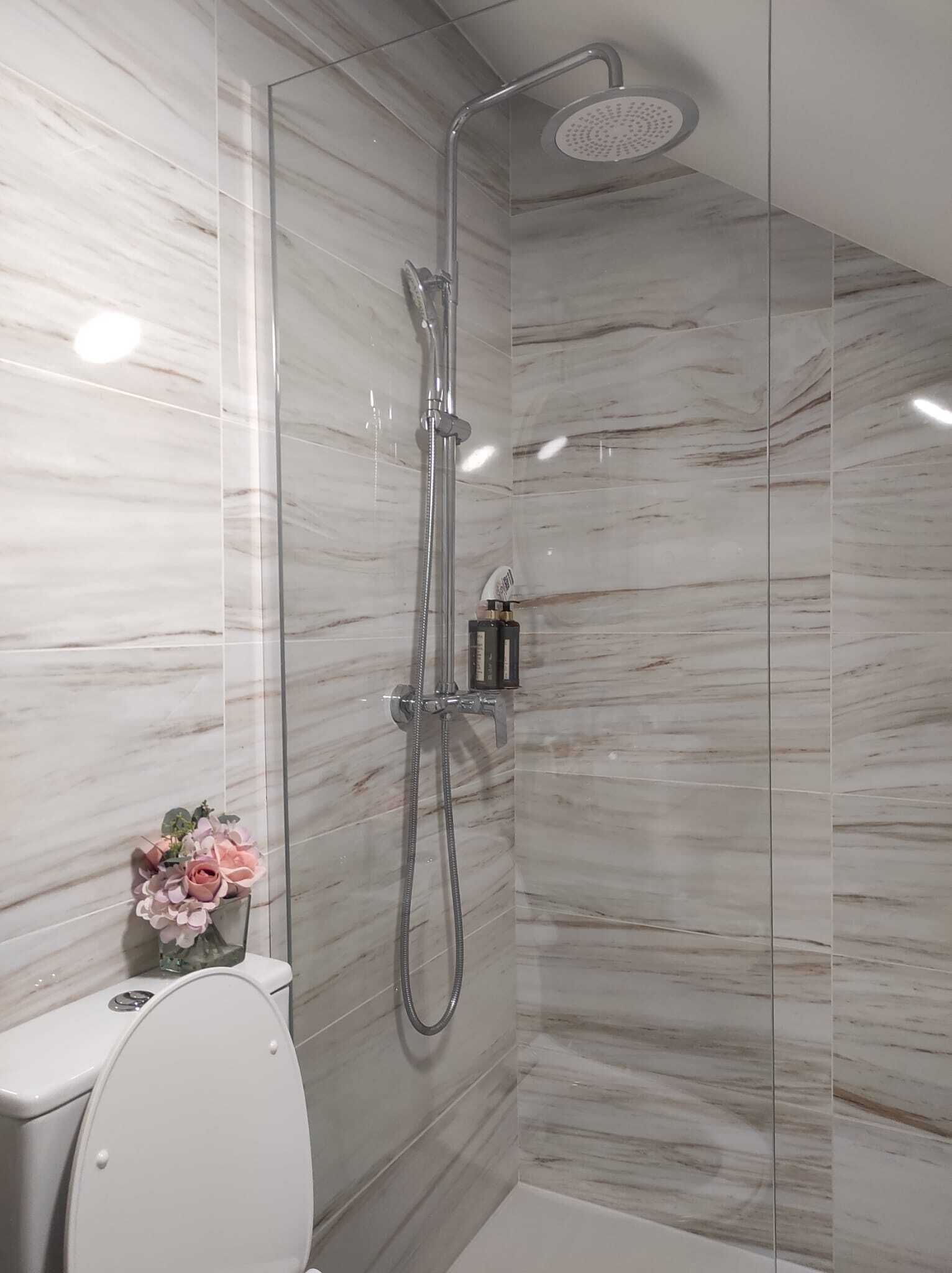 A modern bathroom with a shower, toilet, and a small vase of flowers.
