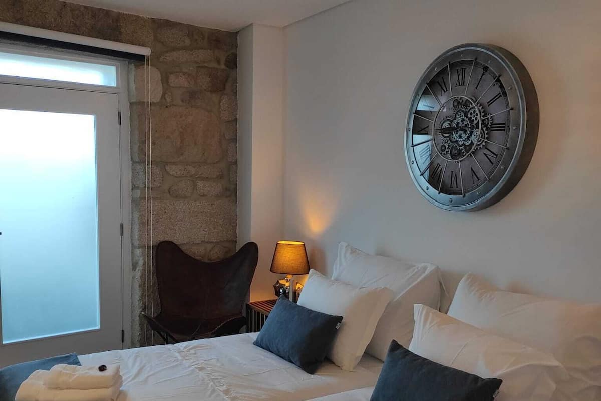 A hotel room with a large bed, two bedside tables, a chair, a lamp, and a wall clock.