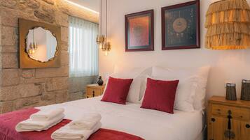 A neatly made bed with white and red bedding, a stone wall, a mirror, and two framed artworks.