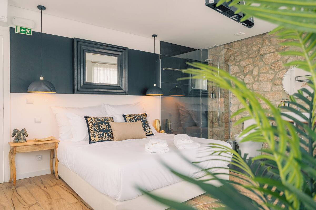 A modern bedroom with a large bed, a stone wall, and a glass shower enclosure.