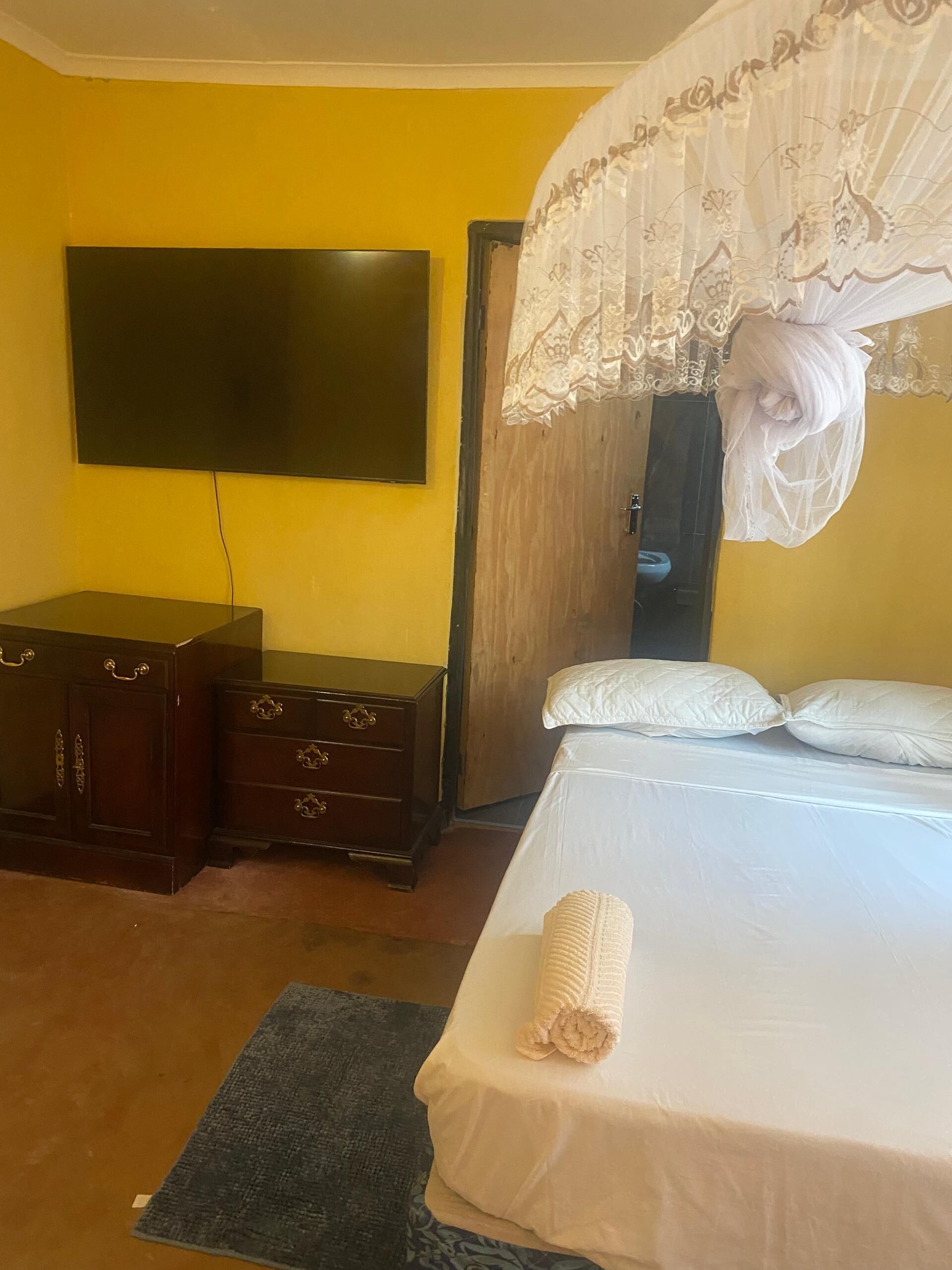 A bedroom with a bed, a TV mounted on the wall, a wooden wardrobe, and a door with a curtain.