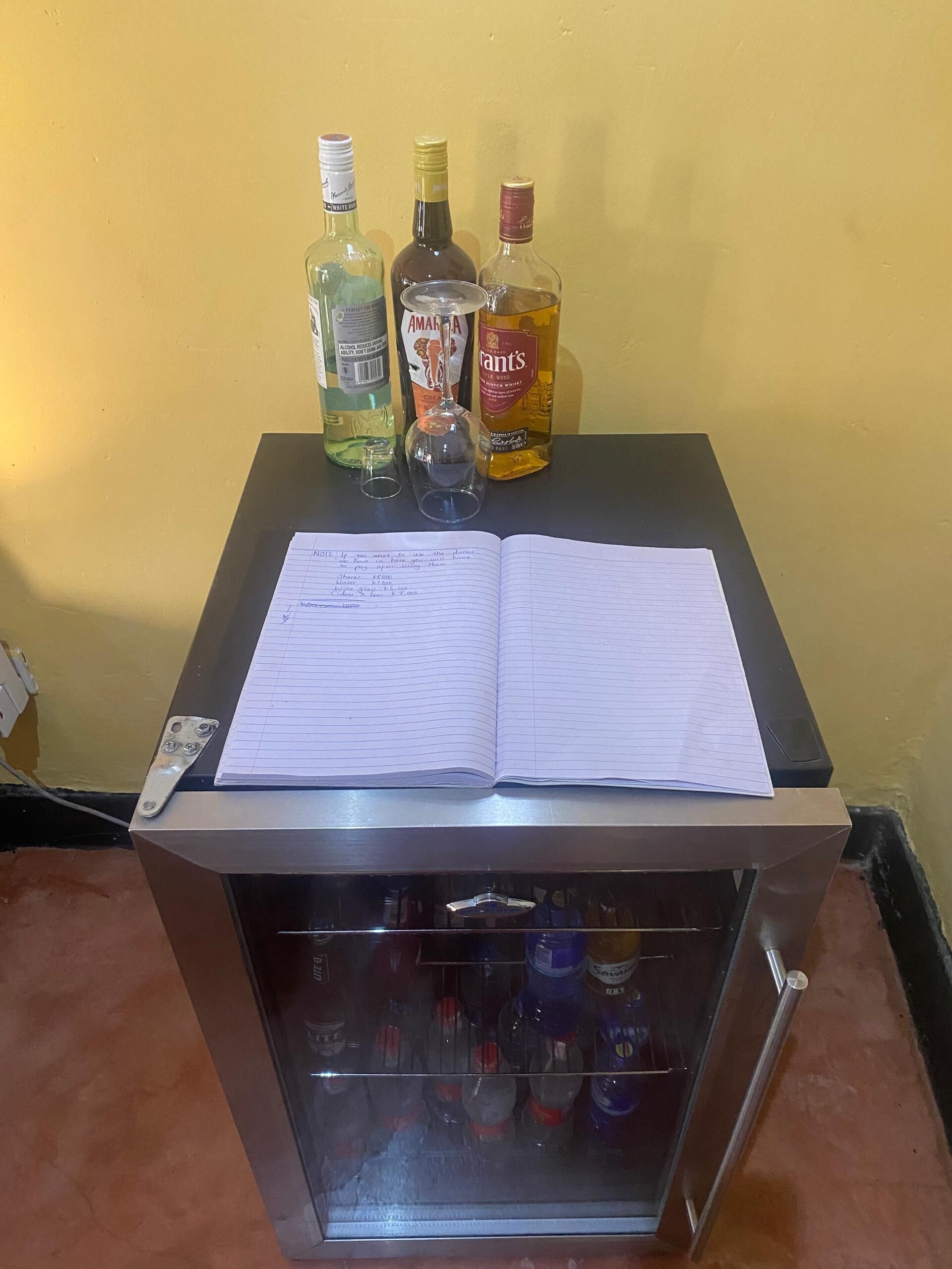 Una mesa con un cuaderno, tres botellas de licor y un vaso.