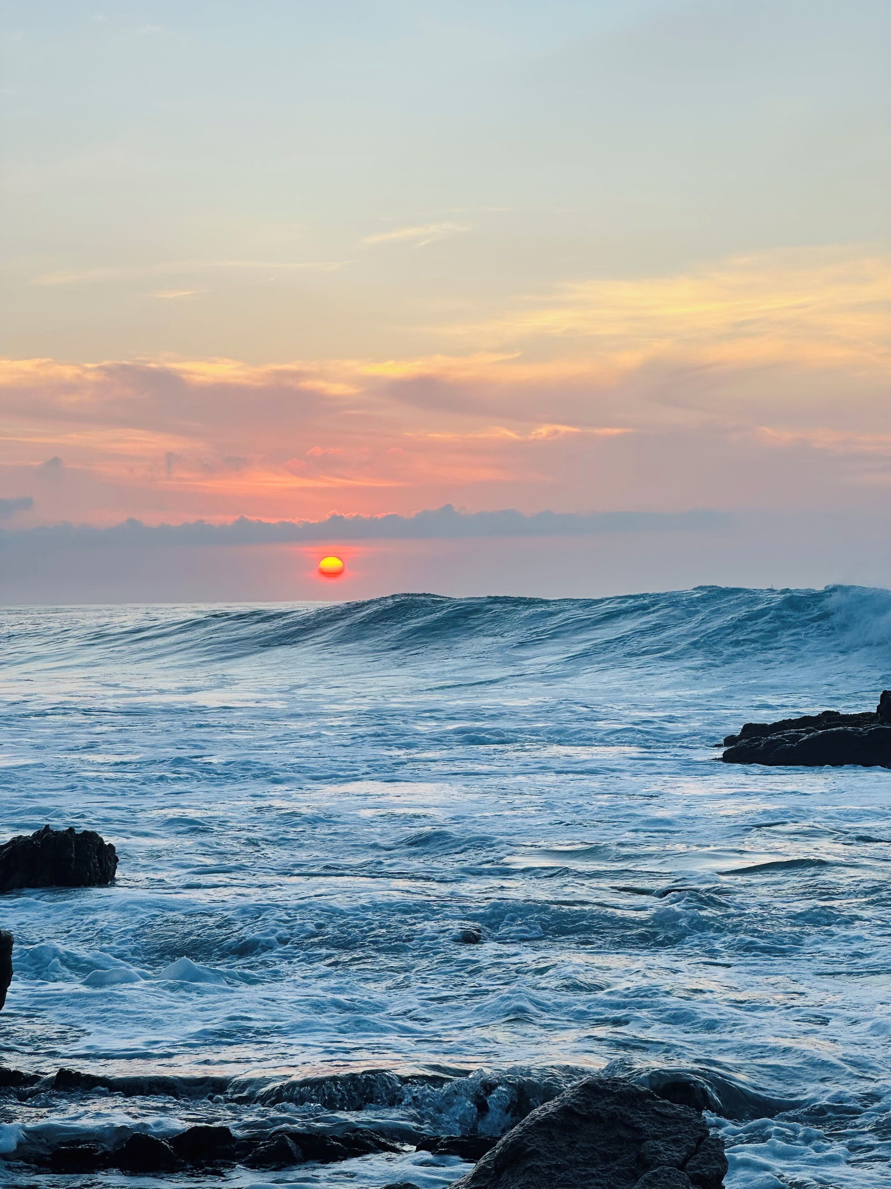 Un coucher de soleil sur l’océan, avec des vagues qui s’écrasent contre les rochers.