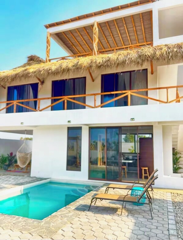 A two-story building with a thatched roof, a swimming pool, and outdoor seating. - Peaceful Beach House in Oaxaca-Surrounded by Nature, Pool, Family & Pet Friendly (Agua Blanca)