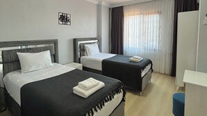 Quarto de hotel com duas camas, uma mesa e um ventilador de teto.