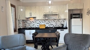 Een moderne keuken met witte kasten, een zwart aanrecht en een ingebouwde oven. Er staat een eettafel met vier stoelen bij, en erboven hangt een kroonluchter.