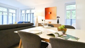 A modern dining area with a table set for two, a sofa, and a window with blinds. - "Relaxed vacation days await you in the apartment Sergio 1 on Norderney!" (Norderney)