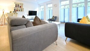 A modern living room with two sofas, a flat-screen TV, a bookshelf, and large windows. - "Relaxed vacation days await you in the apartment Sergio 1 on Norderney!" (Norderney)