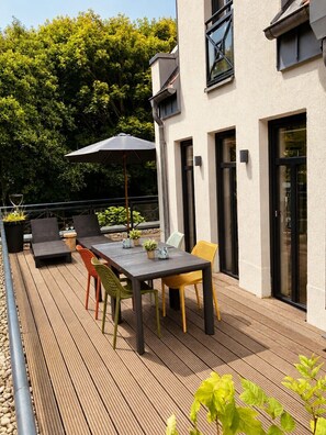 A wooden deck with a table and chairs, a potted plant, and a window overlooking a garden. - "Relax in the apartment Sergio 3: Comfortable vacation apartment on Norderney!" (Norderney)