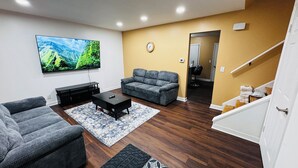 Una sala de estar con una televisión de pantalla plana, dos sofás grises, una mesa de centro y una alfombra estampada.