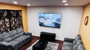 Una sala de estar moderna con un televisor de pantalla plana montado en la pared, dos sofás grises, una mesa de centro negra y una alfombra estampada.