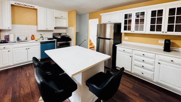 Una cocina moderna con armarios blancos, un refrigerador de acero inoxidable y una isla central con dos sillas negras.