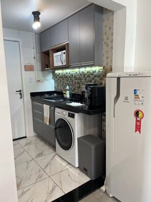 A compact kitchen with a built-in washer, a microwave, and a refrigerator. - Tha flat 311 (Campinas)