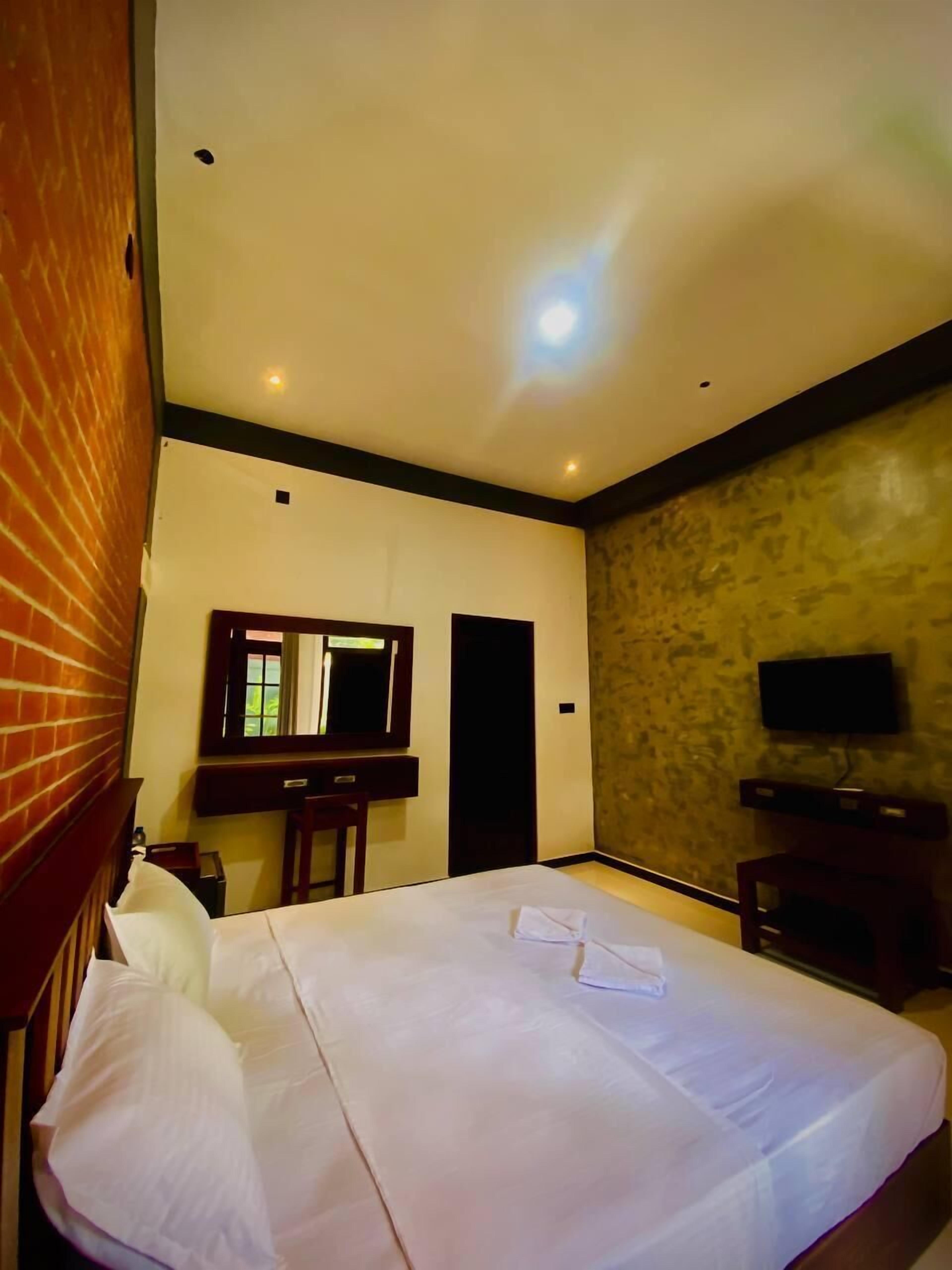 A hotel room with a large bed, a desk, a mirror, and a television.