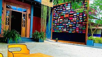 Un edificio con un muro colorido de banderas, mesas al aire libre con sillas amarillas y una banca de madera.