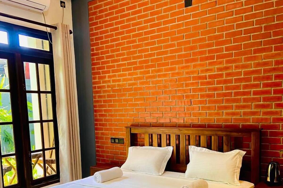 Quarto de hotel com uma cama grande, uma parede de tijolos e uma janela com cortinas.