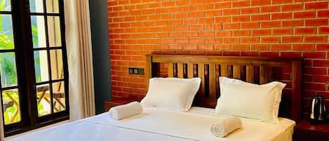 A hotel room with a large bed, a brick wall, and a window with curtains.