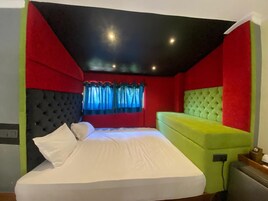 A bedroom with a bed, a headboard, a window with curtains, and a wall with a red and black design.