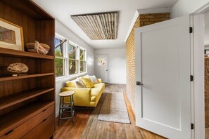 A room with a wooden bookshelf, a yellow sofa, a white door, and a view through a window. - Nucla Haus | In Between Telluride + Moab Basecamp (Nucla)