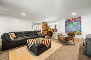 A modern living room with a black leather sofa, a brown leather chair, and a colorful abstract painting on the wall. - Nucla Haus | In Between Telluride + Moab Basecamp (Nucla)