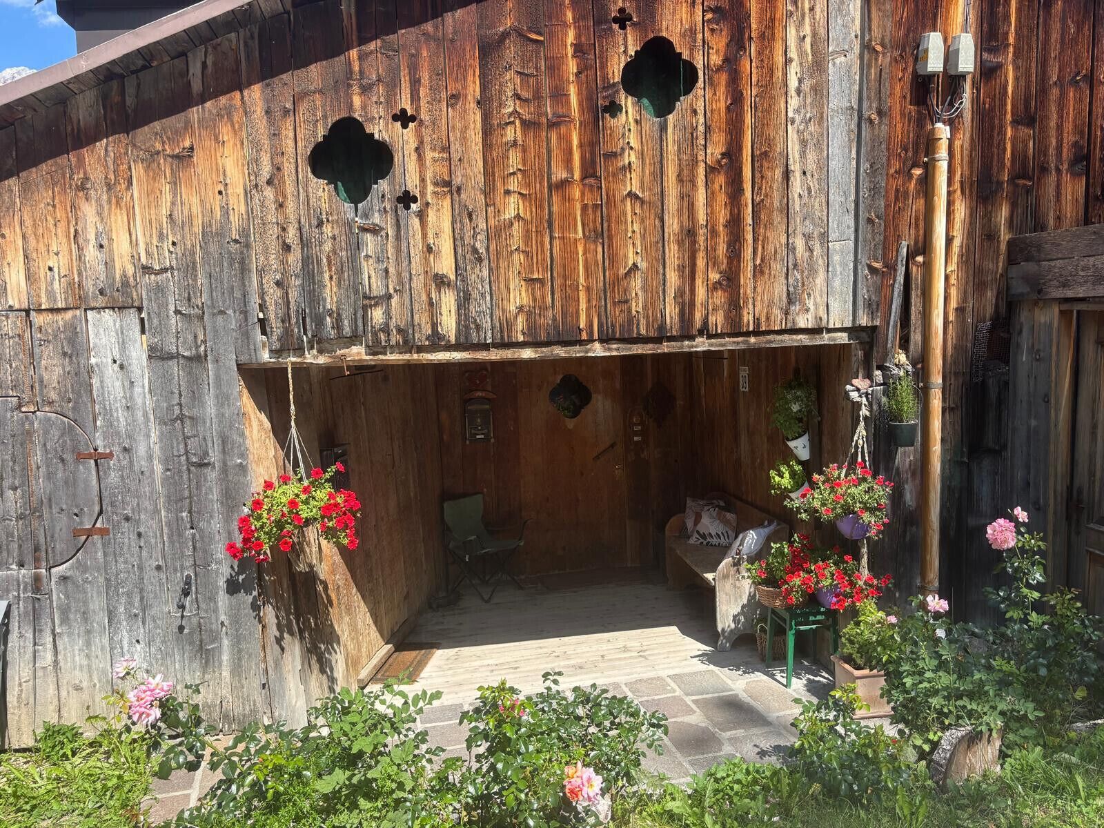 Un bâtiment rustique en bois, doté d’un porche, de plantes en pot et d’un sol en pierre.