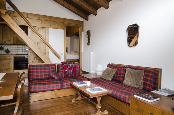 A cozy living area with a wooden staircase, a red plaid sofa, a wooden coffee table, and a white radiator.