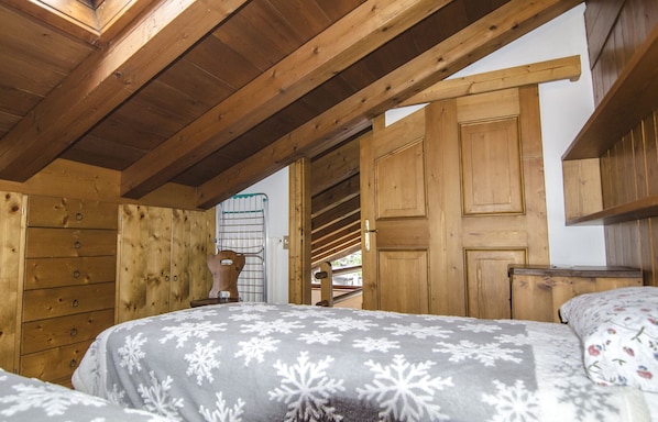 Une chambre dans une cabane en bois, avec un lit, une chaise et une porte en bois.