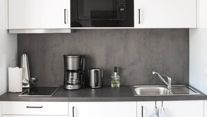 A modern kitchen with white cabinets, a black microwave, a coffee maker, a kettle, and a sink.