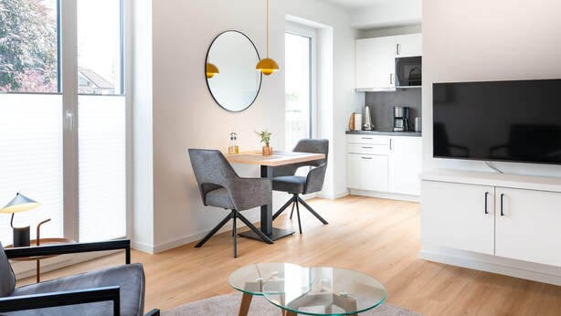 A modern kitchen with white cabinets, a black countertop, and a large flat-screen TV.