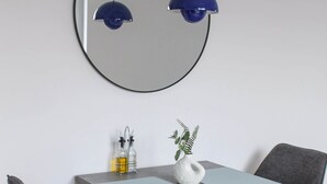 Un área de comedor moderna con una mesa redonda, dos sillas grises, un jarrón blanco con una planta y dos lámparas colgantes azules.