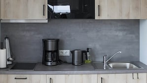 Una cocina moderna con armarios de madera clara, un microondas negro, una cafetera, un hervidor y un lavamanos.
