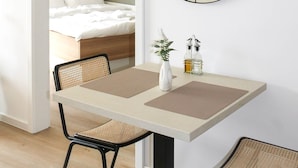 A modern room with a bed, a dining table with chairs, a round mirror, and a hanging light fixture.