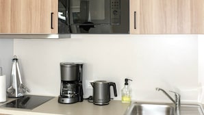 A modern kitchen with wooden cabinets, a black microwave, a coffee maker, and a sink.
