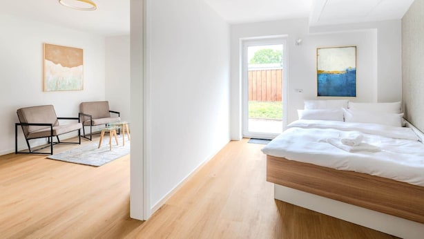 A modern bedroom with a wooden bed, a glass coffee table, two chairs, and a view of the outdoors.