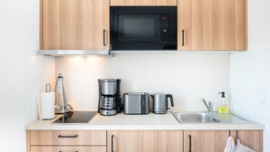 A modern kitchen with wooden cabinets, a black microwave, a coffee maker, a toaster, and a sink with a soap dispenser. - Osternburg (Oldenburg)
